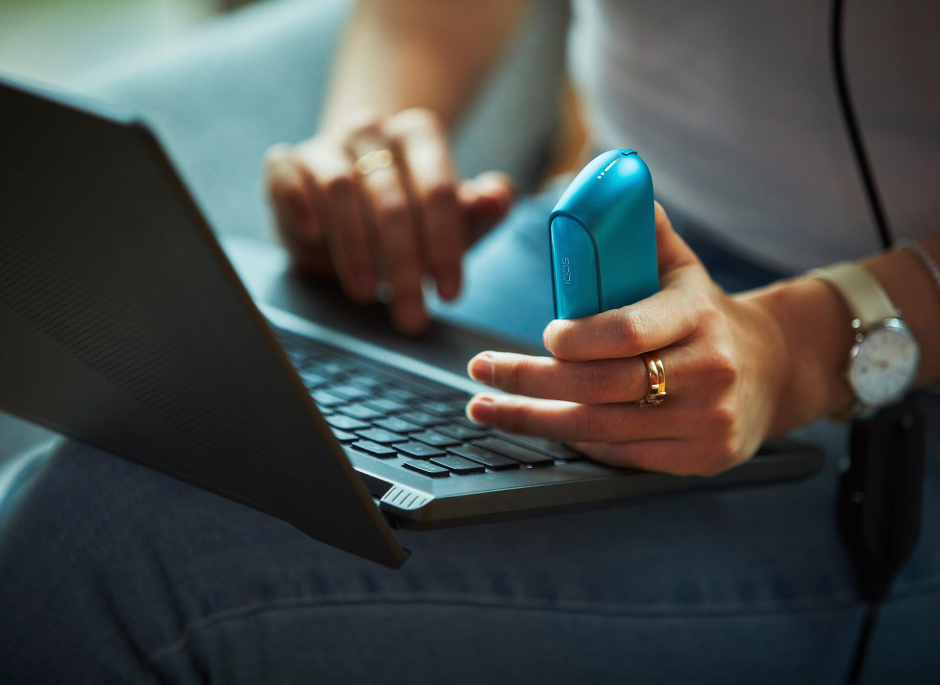 IQOS w dłoni osoby korzystającej z laptopa