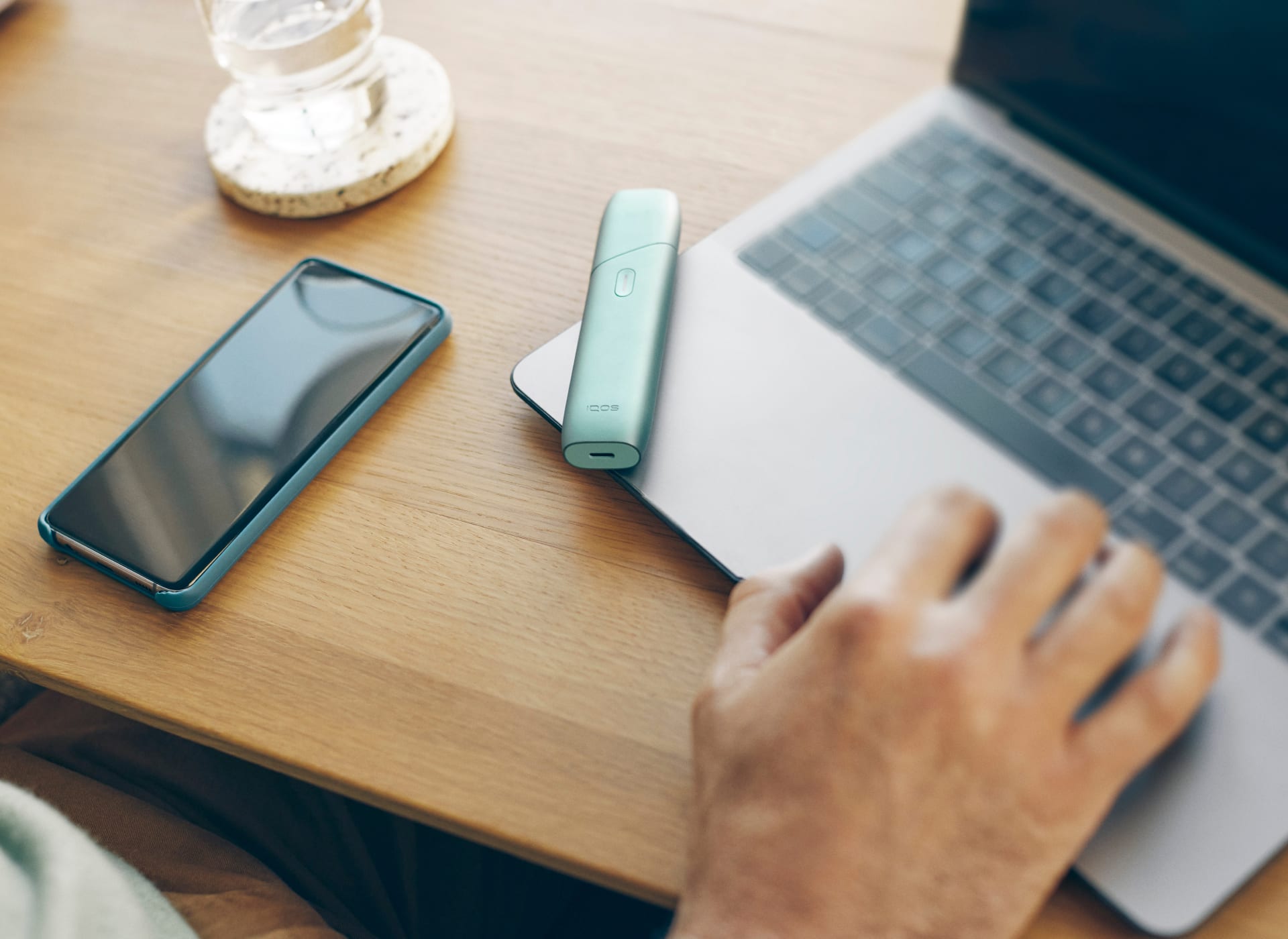 Podgrzewacz IQOS ILUMA ONE leżący na laptopie obok telefonu