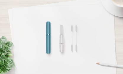 Podgrzewacz IQOS ORIGINALS DUO leżący obok czyścika I patyczków czyszczących