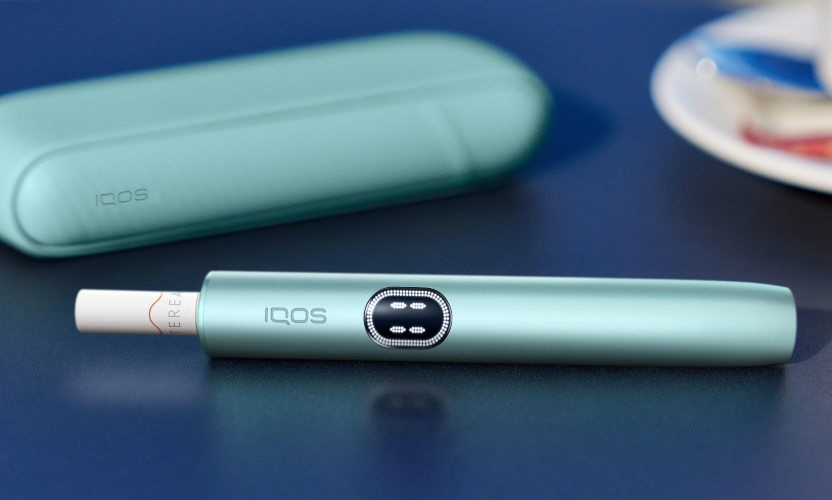 Podgrzewacz IQOS ILUMA i z włożónym wkładem tytoniowym leżący obok przenośnej ładowarki