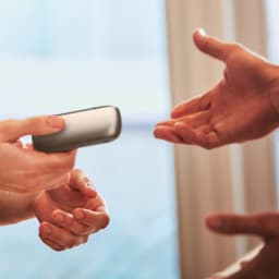 Hands exchanging IQOS Originals Duo pocket charger in Brilliant Gold color.