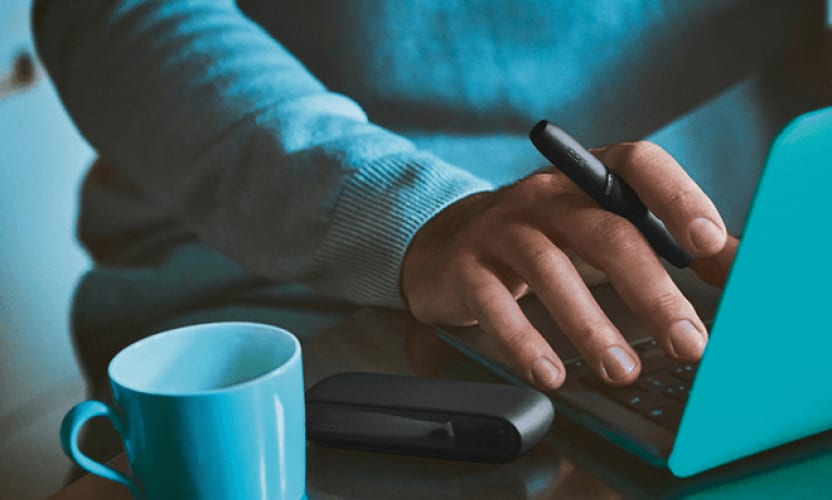 Podgrzewacz IQOS ILUMA w dłoni osoby piszącej na laptopie
