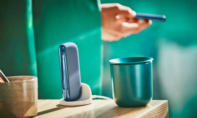 IQOS ILUMA ładuje się w stacji ładującej stojącej obok pojemnika na zużyte wkłady tytoniowe