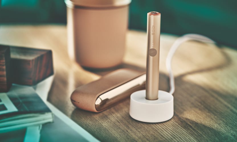 Podgrzewacz IQOS ILUMA w stacji ładującej stojącej obok przenośnej ładowarki