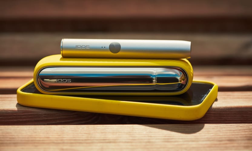 Podgrzewacz IQOS ILUMA I przenośna ładowarka leżące na telefonie