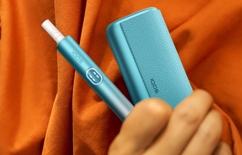 Podgrzewacz IQOS ILUMA i PRIME z włożonym wkładem tytoniowym i przenośna ładowarka trzymane w dłoni
