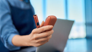 Podgrzewacz IQOS ILUMA i z przenośną ładowarką trzymane w dłoni