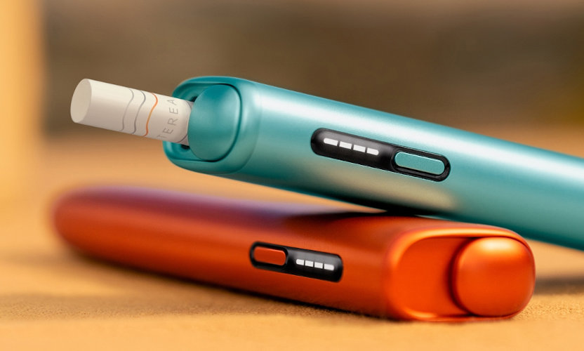 Dwa podgrzewacze IQOS ILUMA i ONE, w kolorach niebieskim i czerwonym, w jednym z podgrzewaczy włożony wkład tytoniowy