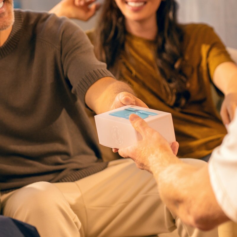 Mężczyzna przekazuje drugiemu mężczyźnie białe pudełko z IQOS-em ILUMA i